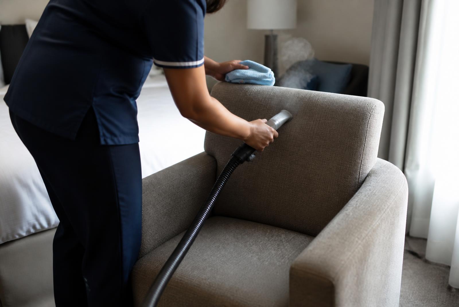 Medewerker stoomt een gestoffeerde fauteuil in een hotelkamer